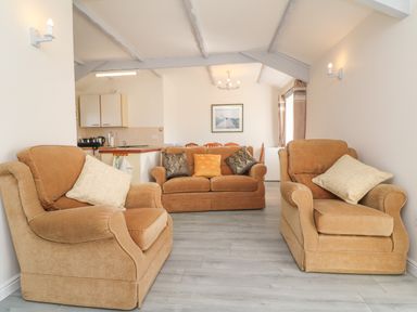A living room with two armchairs and a sofa with cushions next to a kitchen area at The Cottage Chilsworthy near Holsworthy