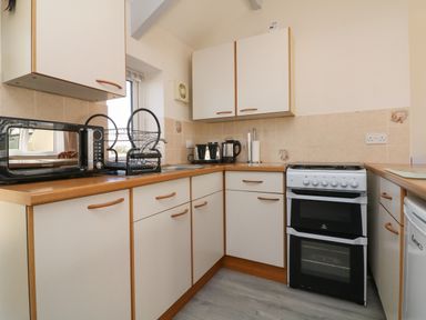 A kitchen with white cabinets a microwave dish rack kettle toaster and stove at The Cottage in Chilsworthy near Holsworthy