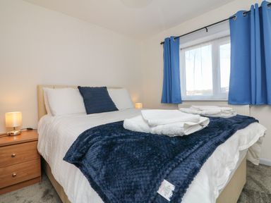 A bedroom with a double bed blue throw and pillows bedside tables with lamps and blue curtains at The Cottage in Chilsworthy near Holsworthy