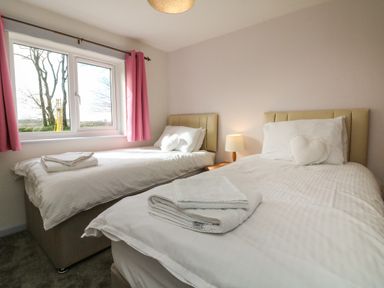 A bedroom with two single beds a bedside table and a window with pink curtains at The Cottage in Chilsworthy near Holsworthy