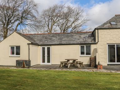 An exterior view of a house with a bench and table on a patio and leafless trees in the background at The Cottage in Chilsworthy near Holsworthy