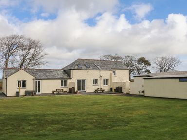 The back of a light-colored house with two picnic tables on a patio and a large green lawn at The Cottage in Chilsworthy near Holsworthy