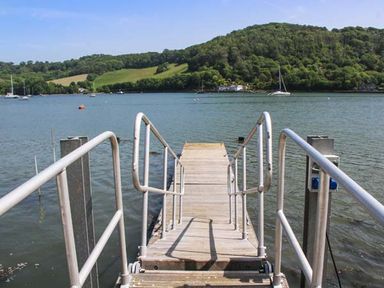A dock with metal railings leading to a body of water with boats and forested hills in the background at Ancarva Near Kingsands
