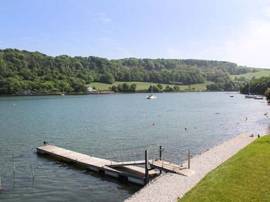 A wooden dock on a river with grassy bank and trees on hills in the background at Ancarva Near Kingsands