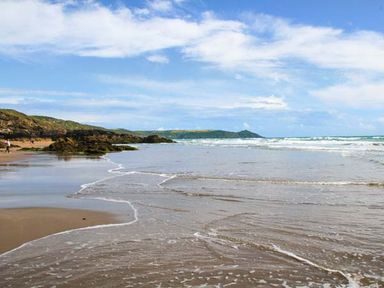 A beach with waves washing onto the shore and rocky cliffs in the background at Ancarva Near Kingsands
