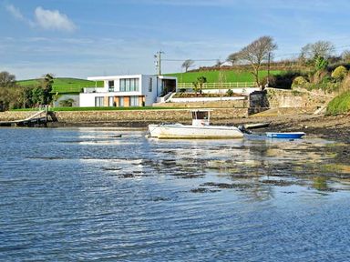 A modern white house near a shoreline with boats on water at Ancarva Near Kingsands