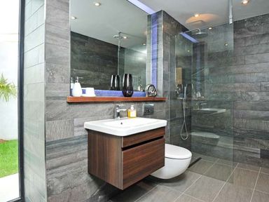 A bathroom with a sink, wooden cabinet, toilet, glass shower enclosure, and large mirror at Ancarva Near Kingsands