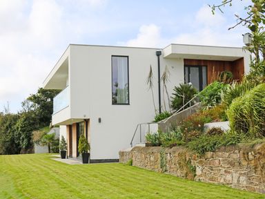 A modern two-story house with white walls, large windows, balcony, and a garden with grass and plants at Ancarva Near Kingsands