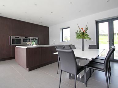 A kitchen with dark cabinets island with drinks white dining table with black chairs and a vase with flowers at Ancarva near Kingsands
