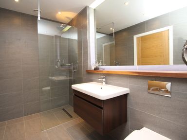 A bathroom with a wall-mounted sink cabinet a large mirror a shower area with glass partition and a wooden door at Ancarva Near Kingsands