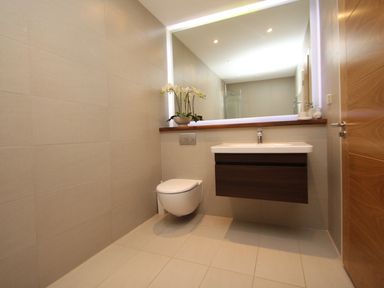 A bathroom with a wall-mounted toilet and sink under a large illuminated mirror at Ancarva Near Kingsands
