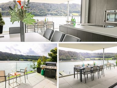 A kitchen with a dining table and chairs overlooking a river and hills with an outdoor balcony with seating and a grill at Ancarva Near Kingsands