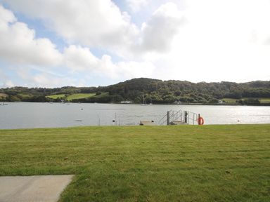 A grassy area leading to a small dock on a body of water with hills and trees in the background at Ancarva Near Kingsands