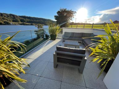 A patio with seating furniture and plants overlooking a body of water at Ancarva Near Kingsands