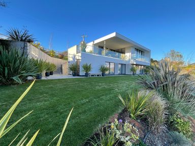 A modern two-story house with glass balcony railings surrounded by a lawn and various plants at Ancarva Near Kingsands