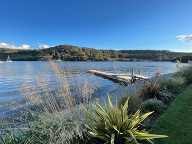 A wooden dock extending into a lake with plants and grass along the shore at Ancarva Near Kingsands