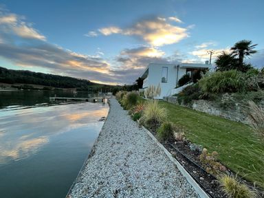 A waterfront property with white gravel shore grass and a modern white house at Ancarva Near Kingsands