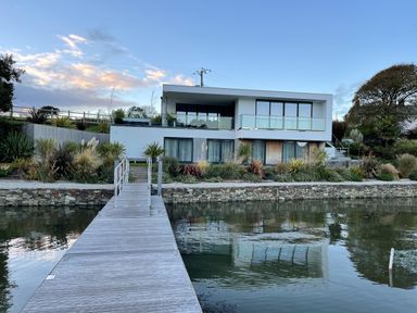 A house with large windows and a balcony by the water with a wooden dock leading to it at Ancarva Near Kingsands