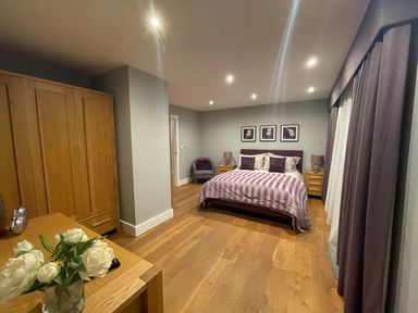 A bedroom with a bed table lamps wardrobe chair flowers and purple curtains at Ancarva Near Kingsands