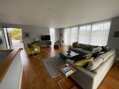 A living room with sofas a cabinet television and large windows with sheer curtains at Ancarva Near Kingsands