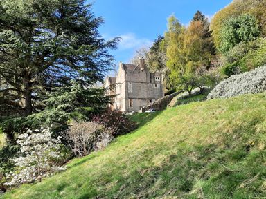 A stone house on a hillside surrounded by trees and shrubs at Haslington House in Malvern