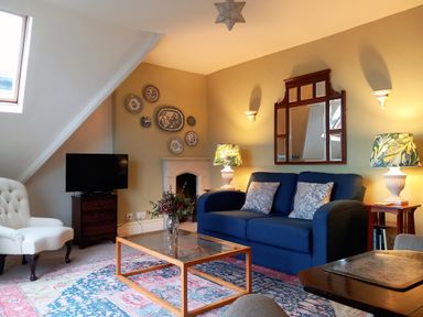 A living room with a blue sofa two patterned lamps a glass coffee table and a white armchair at Haslington House in Malvern