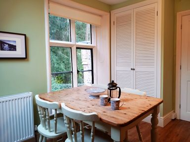 A dining area with a wooden table and four chairs near a window and a closet at Haslington House in Malvern