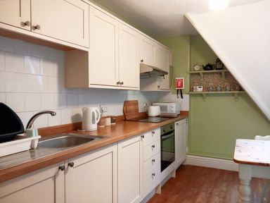 A kitchen with white cabinets a wooden countertop a sink kettle toaster microwave and shelves at Haslington House in Malvern