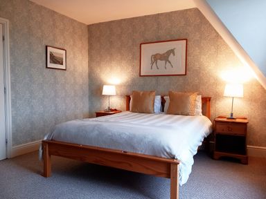 A bedroom with a wooden bed with white bedding and two beige pillows two bedside tables with lamps and framed pictures on the walls at Haslington House in Malvern