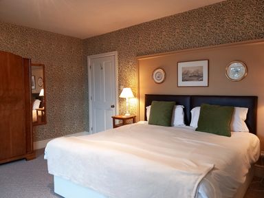 A bedroom with double bed green pillows a wooden wardrobe and wallpaper at Haslington House Malvern