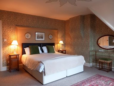 A bedroom with a double bed two bedside tables with lamps a patterned wallpaper and a dressing table with a mirror at Haslington House in Malvern