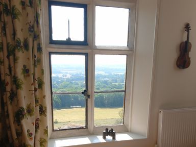 A window with floral curtains binoculars on the sill a violin on the wall and a radiator at Haslington House in Malvern