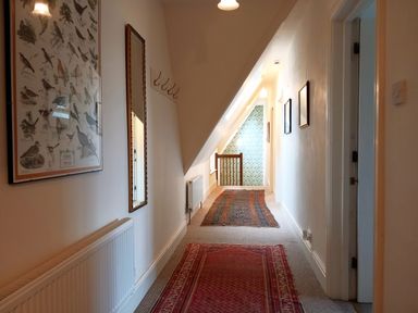 A hallway with hanging hooks a mirror framed pictures and two rugs on the carpet at Haslington House Malvern