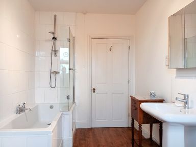 A bathroom with a bathtub with shower head sink and wooden cabinet at Haslington House in Malvern
