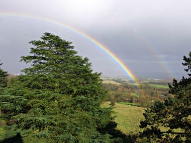 A landscape with large trees and a double rainbow over fields at Haslington House in Malvern