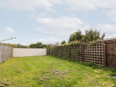 A small garden with grass and wooden fences with lattice panels at Honeysuckle Cottage in Ashwater near Holsworthy
