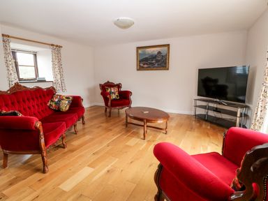 A living room with red velvet sofa chairs wooden coffee table and a television at Honeysuckle Cottage in Ashwater near Holsworthy