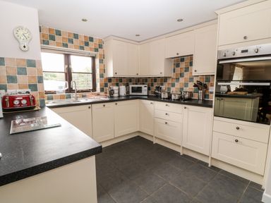 A kitchen with white cabinets black countertops tiled walls and various kitchen appliances at Honeysuckle Cottage in Ashwater near Holsworthy