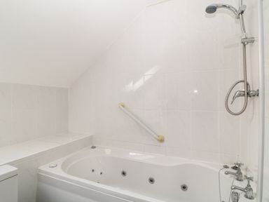 A bathroom with a white bathtub featuring jets a showerhead and tiled walls at Honeysuckle Cottage in Ashwater near Holsworthy