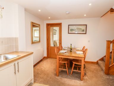 A dining area with a wooden table set for four next to a small kitchen and stairs at The Hayloft in Milton near Brampton