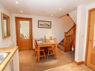 A dining area with a wooden table set for four next to a staircase and wooden doors at The Hayloft in Milton near Brampton
