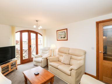 A living room with beige leather sofas a wooden coffee table a lamp a television and wooden arched doors at The Hayloft in Milton near Brampton