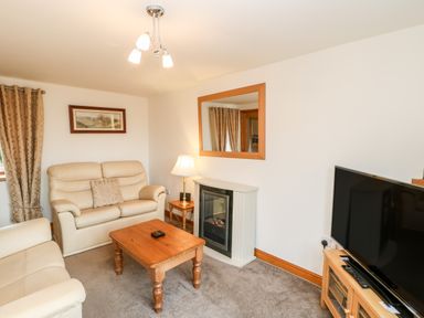 A living room with beige sofas wooden coffee table television and a fireplace at The Hayloft in Milton near Brampton