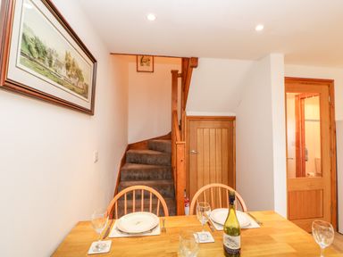 A dining area with a wooden table set with plates and glasses next to carpeted stairs and wooden doors at The Hayloft in Milton near Brampton