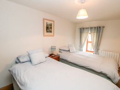 A bedroom with two single beds a bedside table with a lamp a window with curtains and a framed picture on the wall at The Hayloft in Milton near Brampton