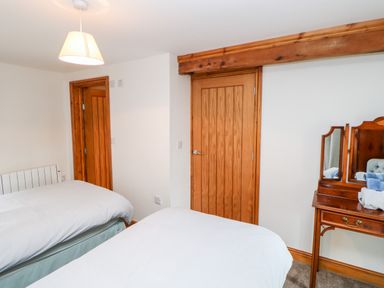 A bedroom with two beds white bedding wooden doors and a wooden dressing table with a mirror at The Hayloft in Milton near Brampton
