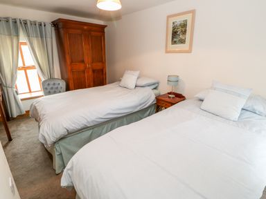 A bedroom with two single beds a wooden wardrobe a bedside table with a lamp and a window with curtains at The Hayloft in Milton near Brampton