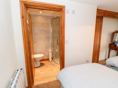 A bedroom with a bed and an open door showing a bathroom with a toilet and shower at The Hayloft in Milton near Brampton