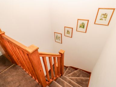 A staircase with wooden railing and carpeted steps with framed pictures on the wall at The Hayloft in Milton near Brampton