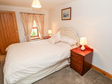 A bedroom with a double bed bedside tables with lamps a window with curtains a wooden door and a framed picture on the wall at The Hayloft in Milton near Brampton